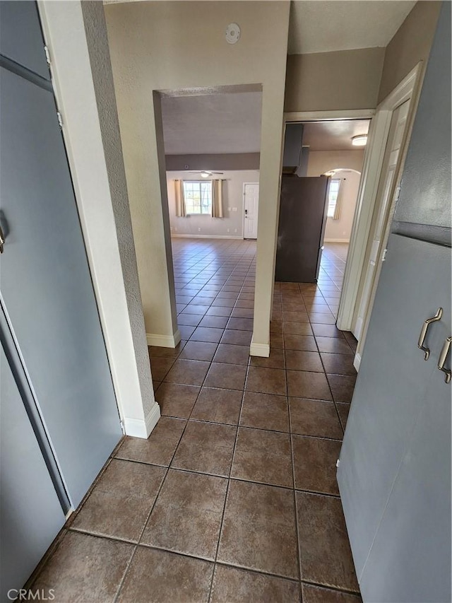 hall featuring baseboards, arched walkways, and dark tile patterned flooring