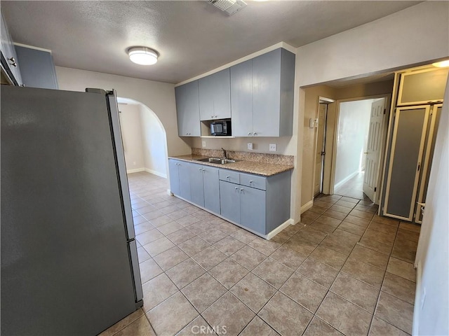 kitchen featuring arched walkways, freestanding refrigerator, light tile patterned flooring, a sink, and black microwave