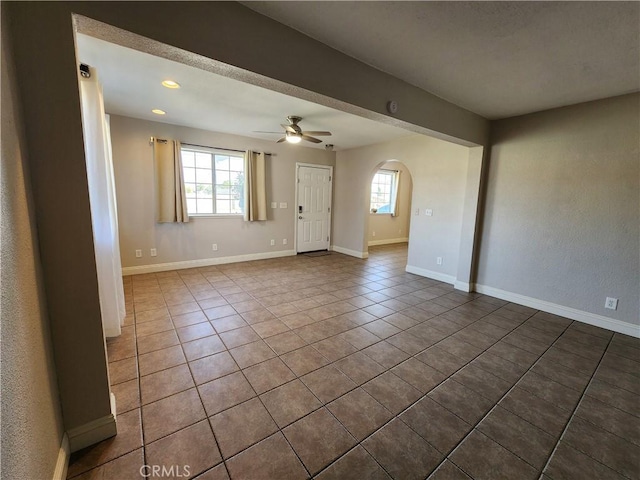 tiled spare room with arched walkways, ceiling fan, plenty of natural light, and baseboards