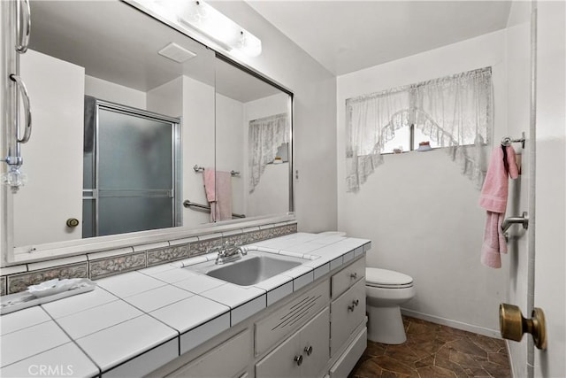 bathroom featuring toilet, stone finish floor, a shower stall, and vanity