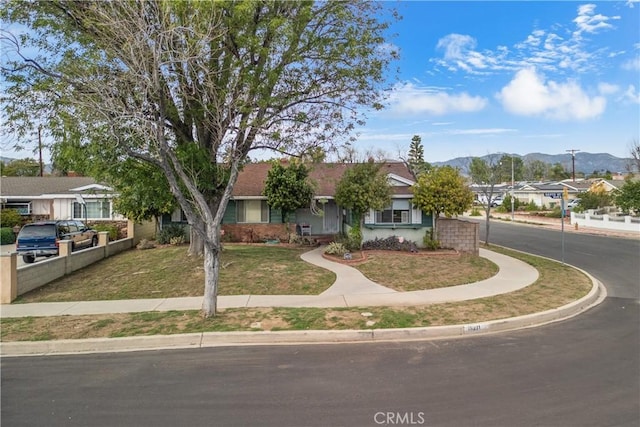 view of front of house with fence, a mountain view, and a front lawn