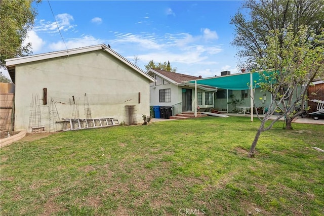 back of house with entry steps, a lawn, and stucco siding