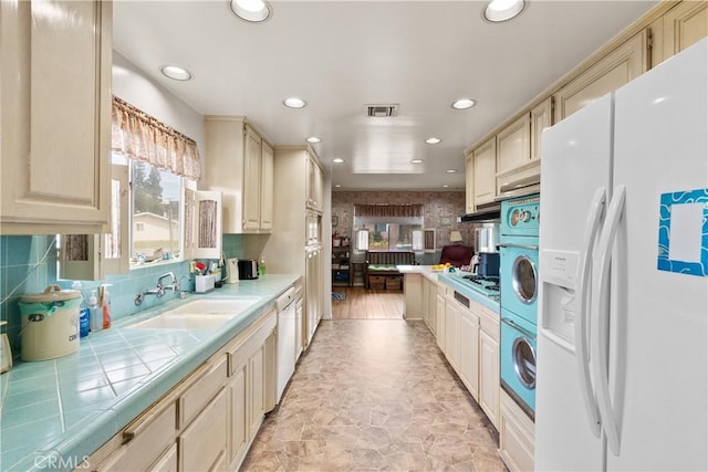 kitchen with tile countertops, white appliances, a sink, visible vents, and stacked washer and clothes dryer