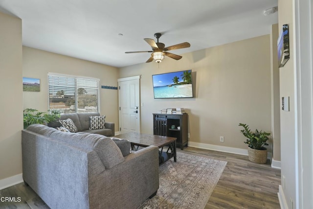 living room with baseboards, dark wood-type flooring, and a ceiling fan