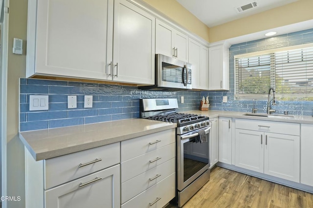 kitchen with visible vents, light wood finished floors, a sink, stainless steel appliances, and white cabinetry