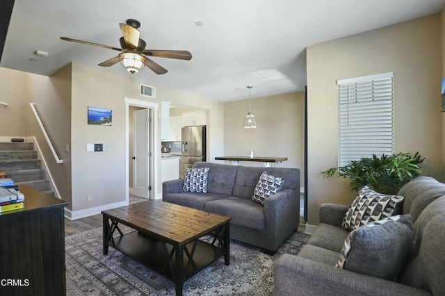 living area featuring wood finished floors, baseboards, visible vents, ceiling fan, and stairs