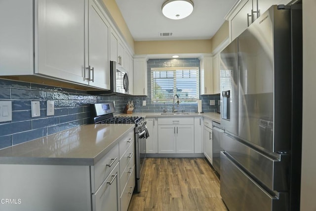 kitchen with backsplash, appliances with stainless steel finishes, wood finished floors, white cabinets, and a sink