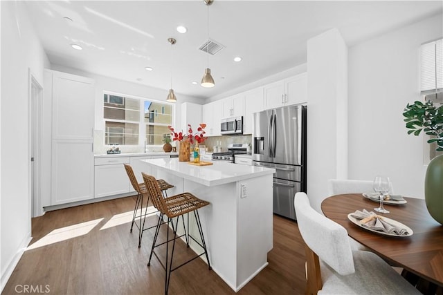 kitchen featuring a breakfast bar area, stainless steel appliances, white cabinetry, visible vents, and a center island