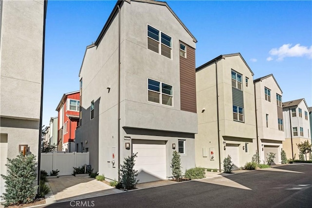 multi unit property with a garage, fence, a residential view, and stucco siding