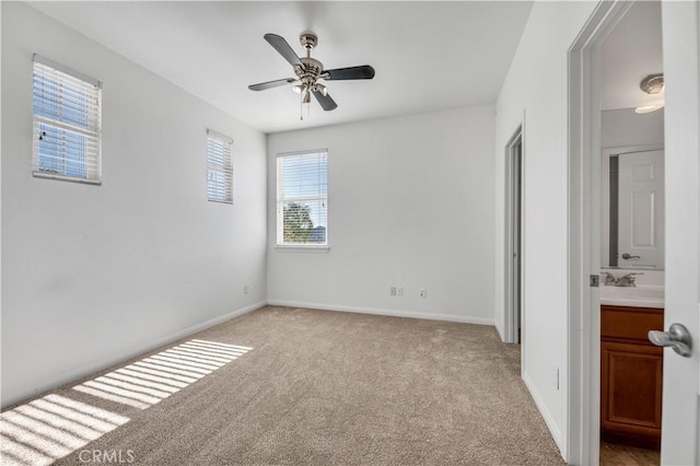 unfurnished bedroom featuring baseboards, a ceiling fan, ensuite bath, carpet flooring, and a sink