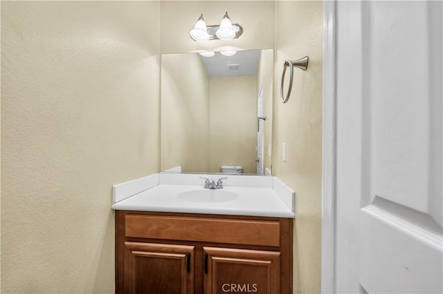 half bath with a textured wall and vanity