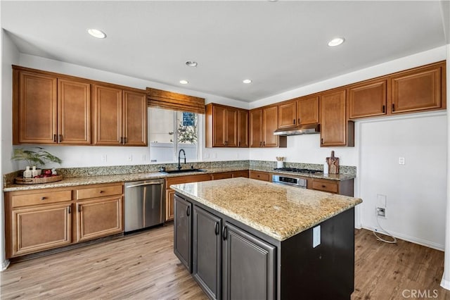 kitchen featuring light wood-style floors, appliances with stainless steel finishes, light stone countertops, under cabinet range hood, and a sink