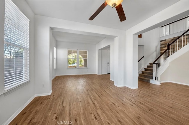 unfurnished living room featuring a ceiling fan, wood finished floors, baseboards, and stairs