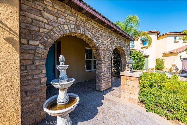 entrance to property with stone siding, a tile roof, and stucco siding