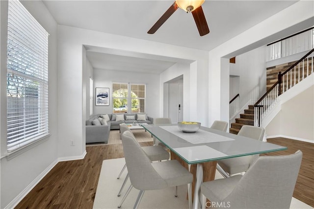 dining area featuring a ceiling fan, baseboards, stairway, and dark wood-type flooring