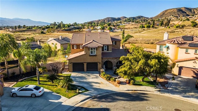 view of front of home with a tiled roof, stone siding, an attached garage, and a mountain view