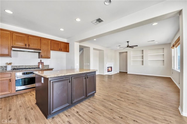 kitchen featuring visible vents, light wood-style flooring, appliances with stainless steel finishes, a glass covered fireplace, and under cabinet range hood