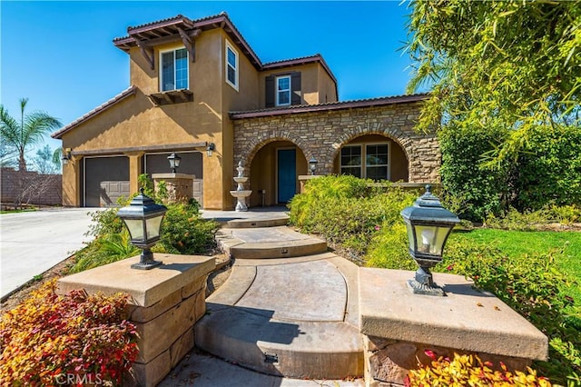 mediterranean / spanish house featuring stone siding, a tile roof, concrete driveway, and stucco siding