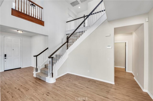 entrance foyer with a towering ceiling, wood finished floors, visible vents, and baseboards