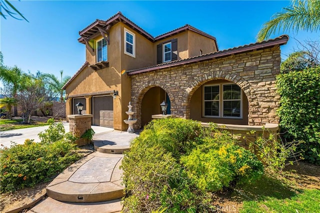 mediterranean / spanish house featuring stucco siding, concrete driveway, a garage, stone siding, and a tiled roof