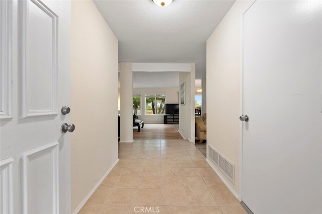 corridor featuring visible vents, a textured ceiling, baseboards, and light tile patterned floors