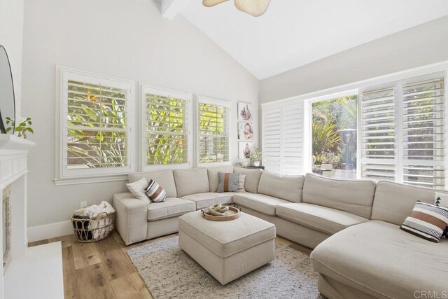 living area with baseboards, a fireplace with flush hearth, beam ceiling, wood finished floors, and high vaulted ceiling