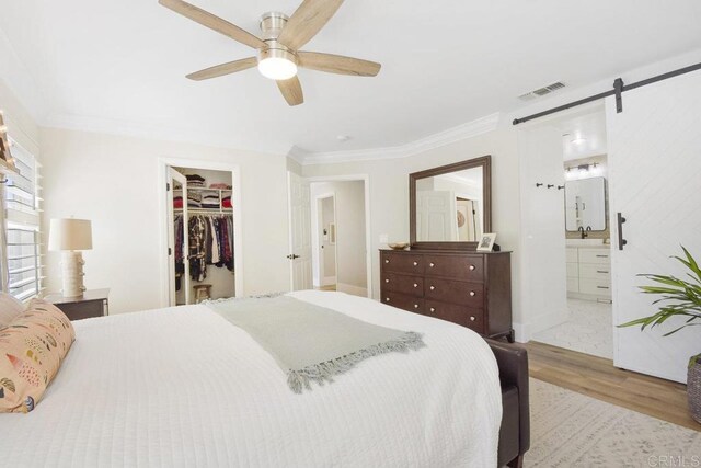 bedroom with visible vents, wood finished floors, a barn door, crown molding, and a spacious closet