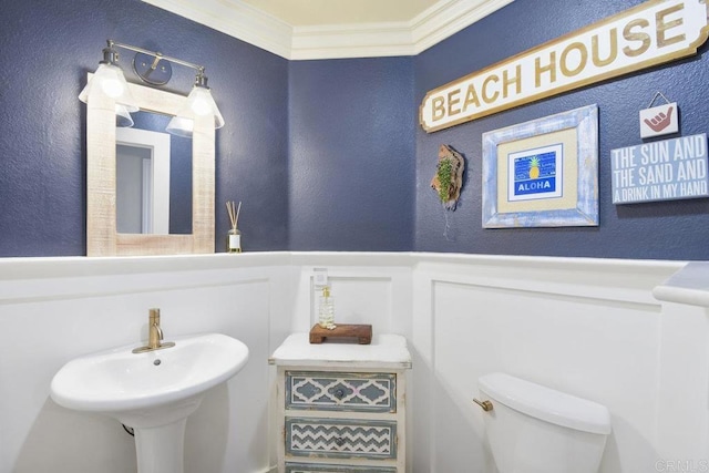 half bath with crown molding, toilet, wainscoting, a textured wall, and a decorative wall