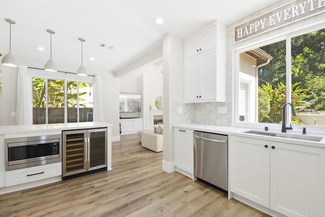 kitchen with a sink, decorative backsplash, wine cooler, light wood-style floors, and appliances with stainless steel finishes