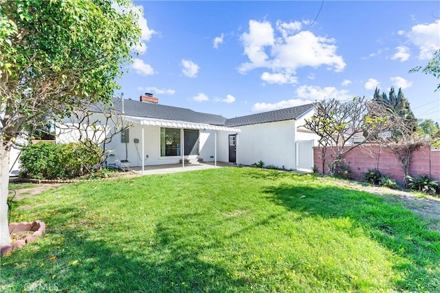 rear view of property featuring a patio, fence, a lawn, stucco siding, and a chimney