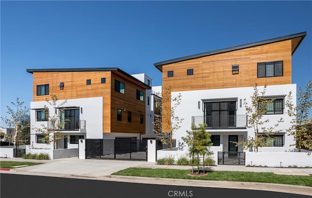 view of front of home featuring an attached garage, a balcony, fence, concrete driveway, and stucco siding