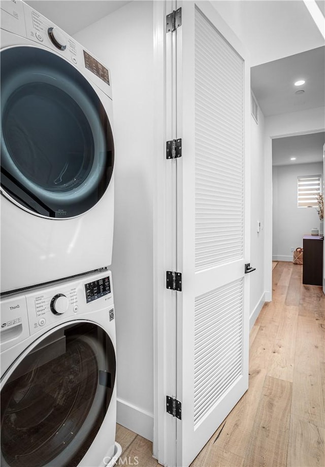 washroom featuring laundry area, stacked washer and dryer, light wood-style flooring, and baseboards