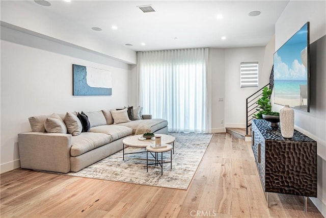 living room featuring recessed lighting, visible vents, light wood-type flooring, baseboards, and stairs