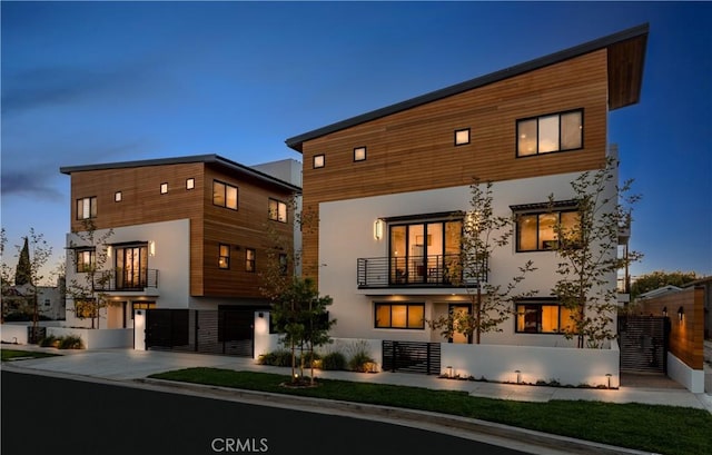 rear view of property featuring driveway, a fenced front yard, a balcony, and stucco siding