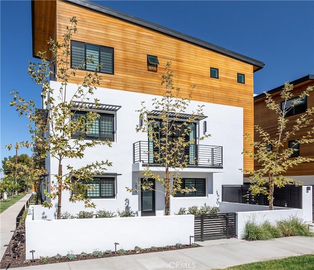 modern home with a balcony, a fenced front yard, and stucco siding