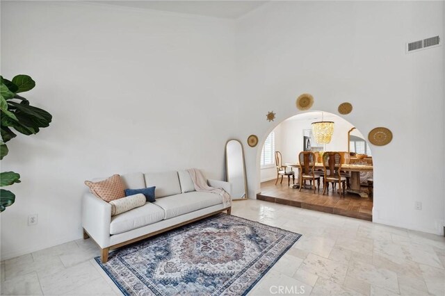 living area featuring arched walkways, stone tile floors, visible vents, a towering ceiling, and baseboards