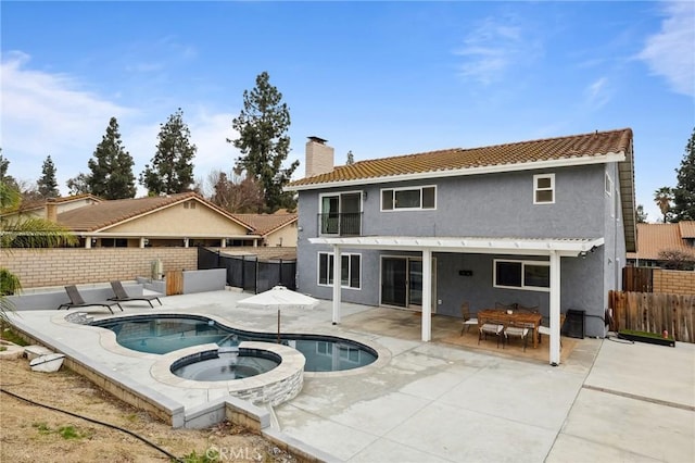 back of house with a patio, a chimney, stucco siding, an in ground hot tub, and a fenced backyard