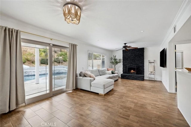 living area with visible vents, ornamental molding, a ceiling fan, a stone fireplace, and wood finished floors