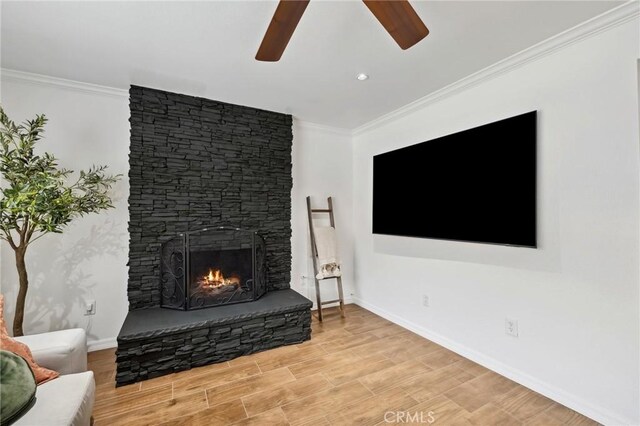 living area featuring a fireplace, wood finished floors, a ceiling fan, baseboards, and crown molding