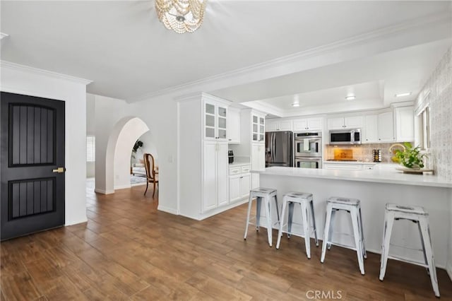 kitchen with stainless steel appliances, a peninsula, wood finished floors, white cabinets, and a raised ceiling