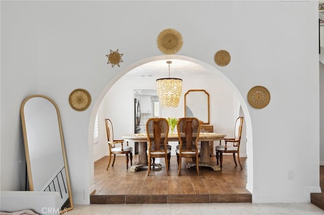 dining space with arched walkways, a notable chandelier, crown molding, and wood finished floors