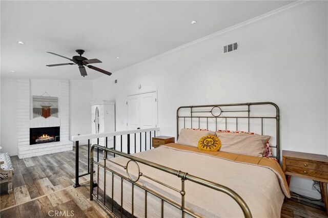 bedroom featuring crown molding, visible vents, a fireplace, and wood finished floors