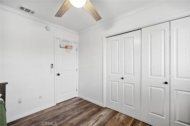 unfurnished bedroom with dark wood-style flooring, crown molding, a closet, visible vents, and baseboards