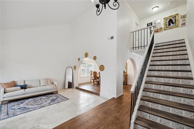 living area featuring arched walkways, crown molding, visible vents, a high ceiling, and stairs