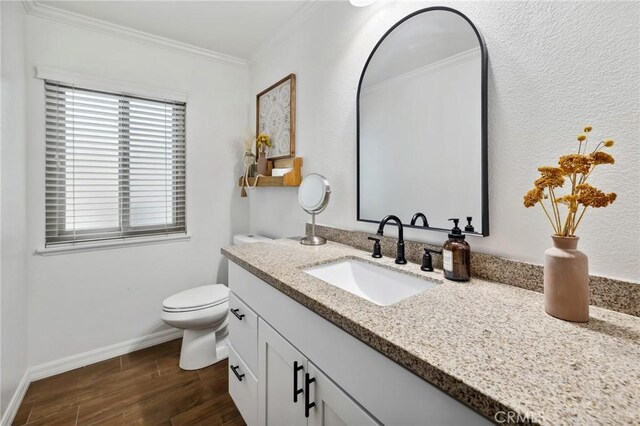 bathroom with toilet, wood finished floors, vanity, baseboards, and crown molding