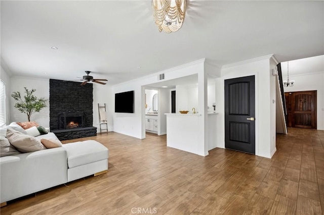 living area with ornamental molding, visible vents, a stone fireplace, and wood finished floors