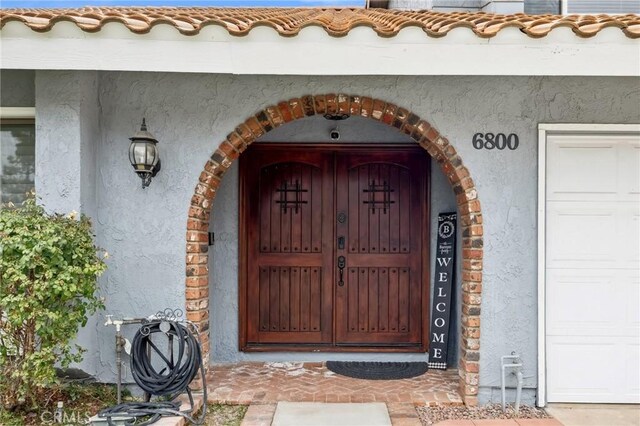 property entrance featuring a garage, a tiled roof, and stucco siding