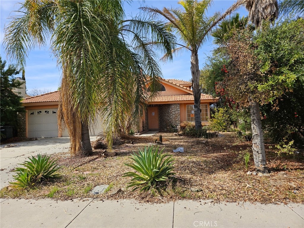 view of property hidden behind natural elements with stucco siding, a garage, stone siding, driveway, and a tiled roof