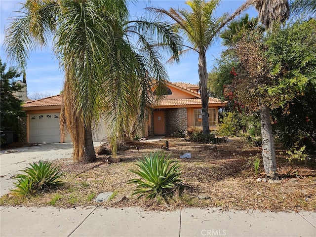 view of property hidden behind natural elements with stucco siding, a garage, stone siding, driveway, and a tiled roof