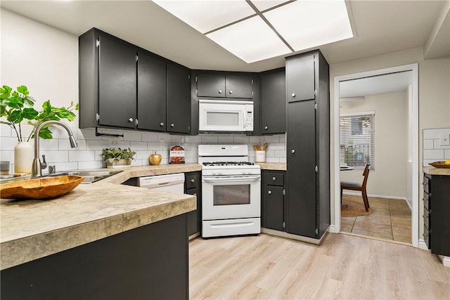 kitchen with white appliances, tasteful backsplash, light wood finished floors, light countertops, and a sink